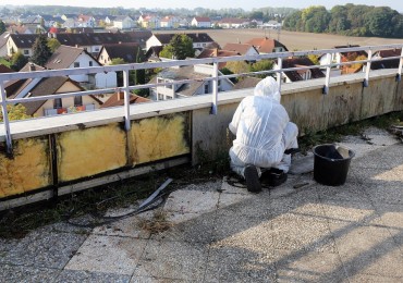Un tecnico specializzato in tuta protettiva sta procedento alla bonifica dell'amianto su un tetto di un'azienda